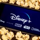 The Disney Plus logo on a phone surrounded by popcorn