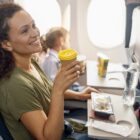 Happy female passenger drinking coffee and smiling while female flight attendant serving lunch on board stock photo