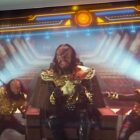 Five people in black and gold Klingon alien costumes dance and sing.