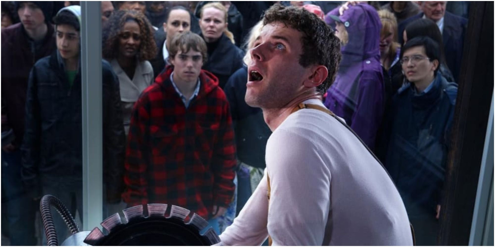 A scared test subject in front of a buzzsaw being watched by a crowd in Saw 3D