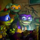 (L to R) April, Leonardo, Michelangelo, Donatello and Raphael in Teenage Mutant Ninja Turtles: Mutant Mayhem, huddled around a phone