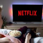 Woman with popcorn bowl holding remote to watch Netflix on television