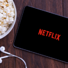 Smartphone displaying Netflix next to bowl of popcorn and ear buds