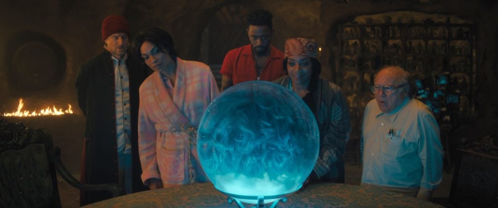 Owen Wilson as Father Kent, Rosario Dawson as Gabbie, LaKeith Stanfield as Ben, Tiffany Haddish as Harriet, and Danny DeVito as Bruce gather around a glowing glass ball in Haunted Mansion