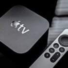 An Apple TV 4K box with a remote next to it, both on a black reflective surface.
