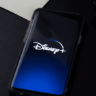 Disney plus on iPhone screen resting on black desk while charging