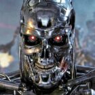 Still from a Terminator movie. A close up of a metal skull with piercing red eyes and teeth. In the background you can see a horde of metal skeletons firing big guns.