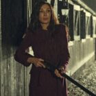 Locked In still image showing Famke Janssen looking scared holding a rifle