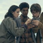Ema, Mickey, and Arthur stare at a mobile phone in Harlan Coben
