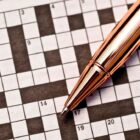 A gold pen on top of an unfinished crossword puzzle