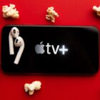 Image showing the Apple TV Plus logo on a mobile phone with a pair of AirPods surrounded by popcorn