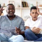 An older man and a boy on a couch looking annoyed and shocked.