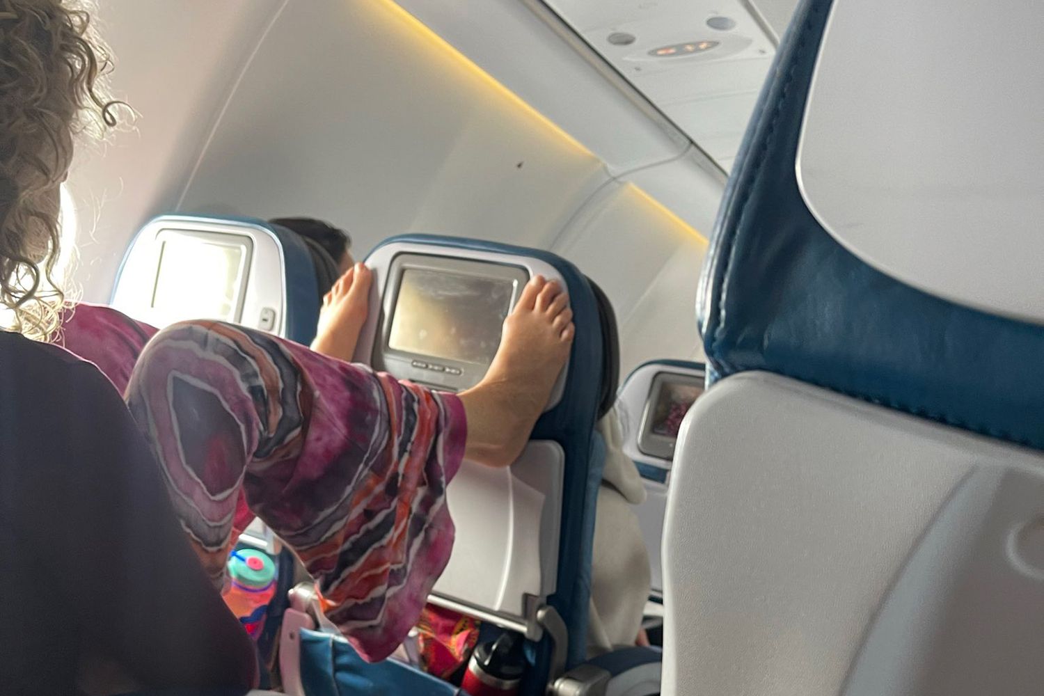 Femme change de chaîne télé avec ses pieds dans l’avion