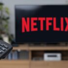 Netflix logo on TV screen with viewer holding remote control