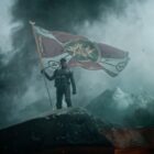 Kora holding a flag aloft in Rebel Moon - Part One: A Child of Fire