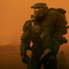 Halo TV series image showing the Master Chief carrying a UNSC Marine over his shoulder in a desolate environment