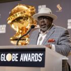 Comedian Cedric the Entertainer, dressed in dapper grey suit and off-white hat, speaks onstage ahead of the 81st Golden Globe Awards