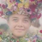 A woman adorned in flowers smiles in this image from A24.