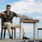 Joe Manganiello sits at a table on the beach with a silver briefcase
