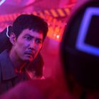A still from the TV series Squid Game (season 2) on Netflix of Lee Jung-jae as Seong Gi-hun surrounded by neon lights.