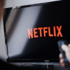 A man watches the Netflix logo on a Toshiba TV with a remote in his hand