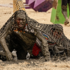 Covered in mud, Survivor 46 castaway Tevin Davis writhes under netting on a beach