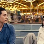 Teo Yoo and Greta Lee as Hae Sung and Na Young in front of a carousel in Past Lives
