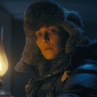 Woman holding a lit lamp. She is wearing a thick winter hat and jacket