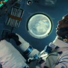 Man inside a space shuttle wearing a white spacesuit.