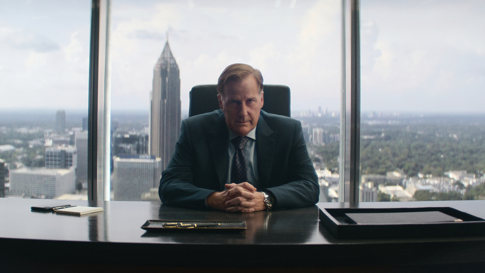 A man sitting at a desk in front of an office window overlooking Atlanta; still from 'A Man in Full'