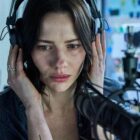 Lily Sullivan listens to someone on headphones in Monolith