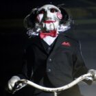 Billy the Puppet stands over the camera with a rope in his hands in the Saw movie
