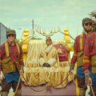 Crystal Fox sits on a sled wearing antlers while being pulled along by men with tartan shirts on in Apple TV Plus