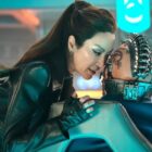 A domineering space woman whispers in the ear of an alien