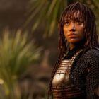 a young woman with braids stands with blurry palm trees in the background
