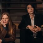 Camille and Issei sit on stairs as they look at something off camera in Drops of God.