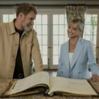 Will Ferrell and Reece Witherspoon stand behind a desk smiling