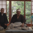 Four Japanese people huddled together on the floor