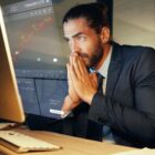 A person looks nervously at a stock chart on a computer screen.