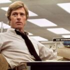 A young Robert Redford sits facing away from a desk