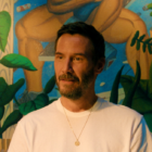 Outcome film review: Keanu Reeves in Jonah Hill's AppleTV movie. Reeves wears a white t-shirt and gold necklace.