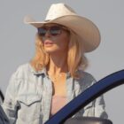 Beth Dutton looks on while standing behind an open car door