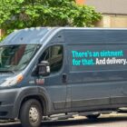 A dark blue Amazon Pharmacy van, parked on the side of the road in front of a short green tree. Text on the van reads, "There's an ointment for that. And delivery."