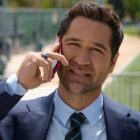 A man takes a call in front of a sports pitch