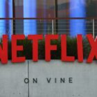 A red "NETFLIX" sign on a concrete wall with "ON VINE" below, surrounded by plants and modern architecture.