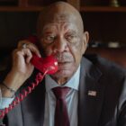 Morgan Freeman speaks into a red corded telephone