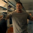 Alan Ritchson as Jack Reacher, holding up his hands on a train.