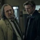 Gary Oldman stands in a dim London office as Jackson Lamb, staring ahead.