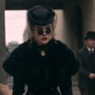 Florence Pugh as Cathy Ames waring a black gown sunglasses and hat as she walks down a street and a man with a bicycle follows her in netflix's east of eden