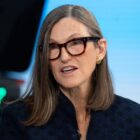 Woman with long gray hair and tortoiseshell glasses speaking in a television studio